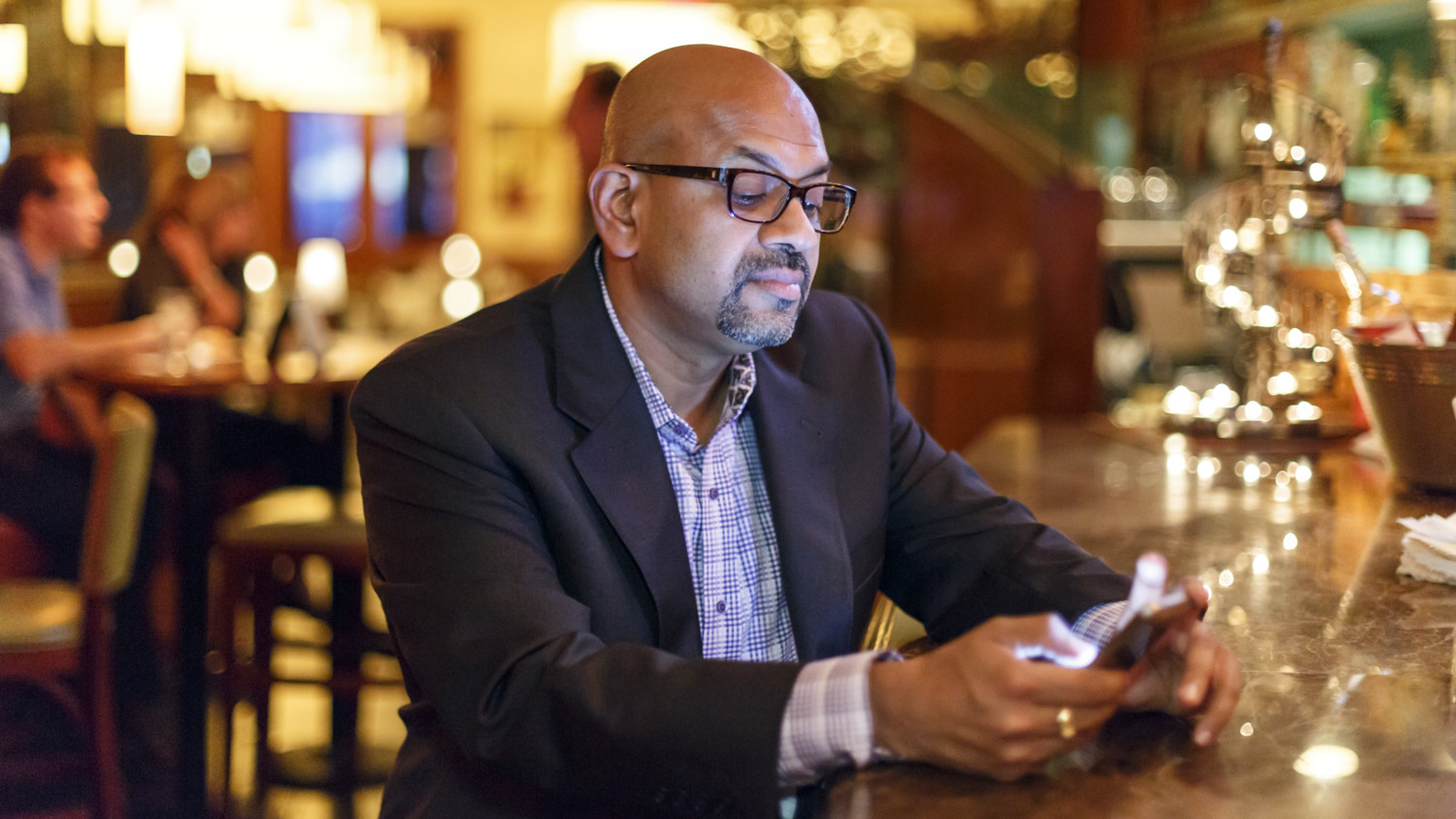 Man in a suit looking at a smartphone at a restaurant bar 
