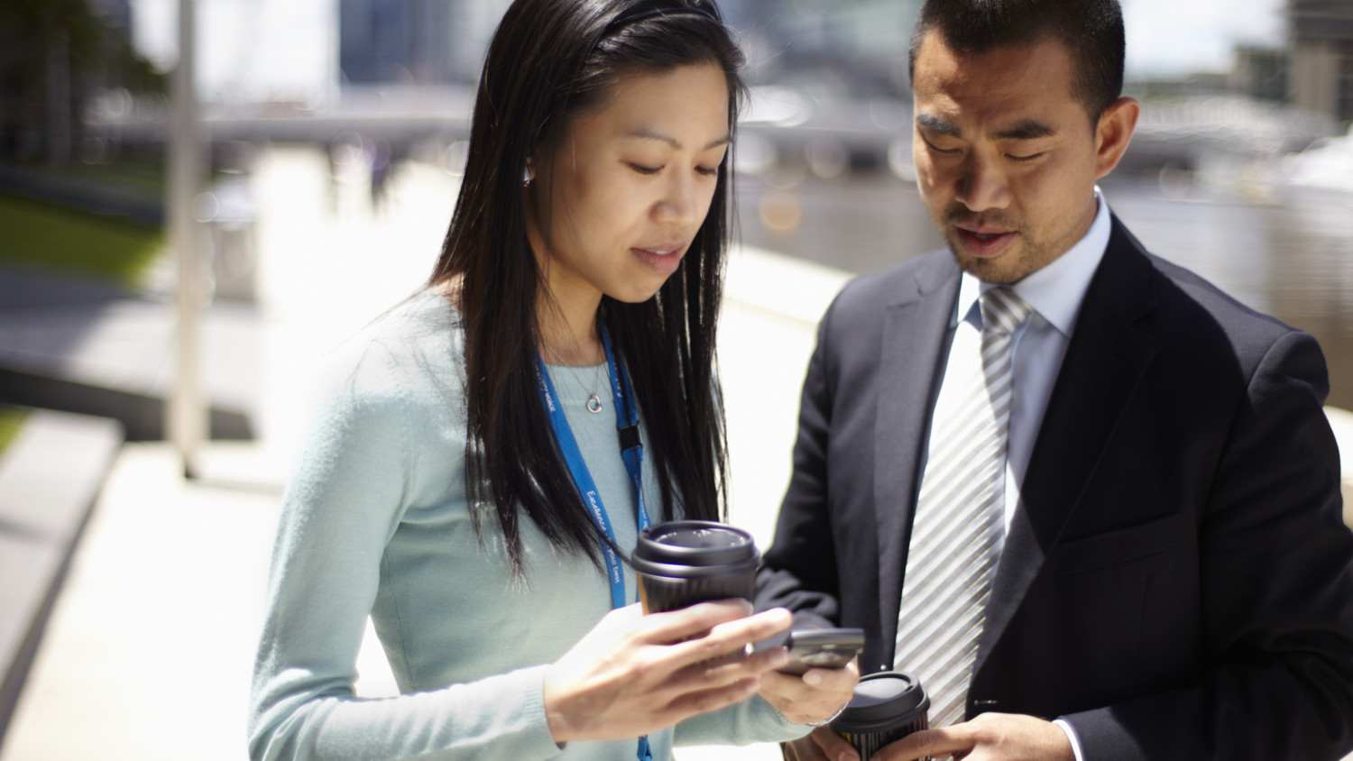 A man and a woman standing outside looking down at their mobile devices