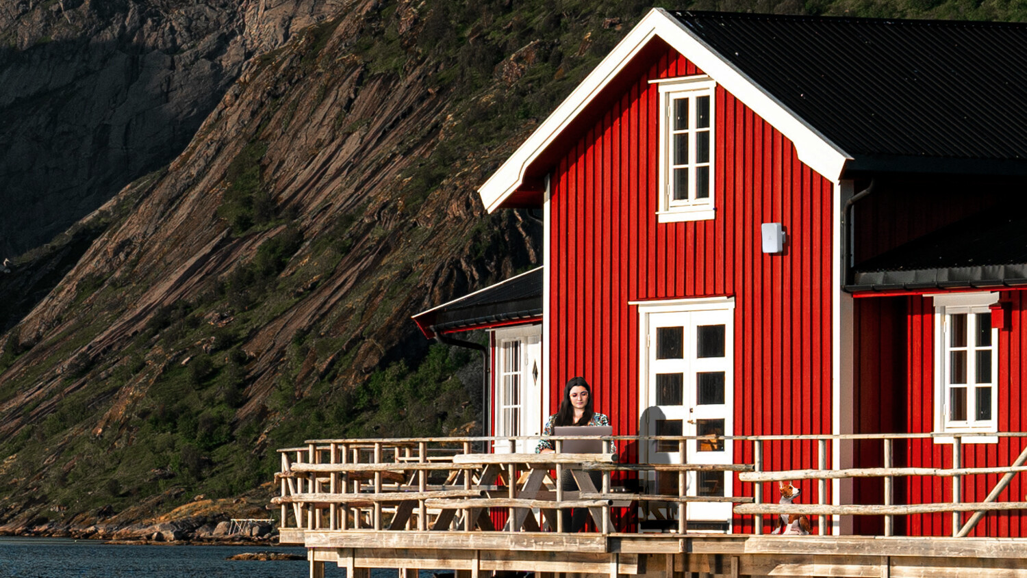 Woman on her computer outside the house next to a lake