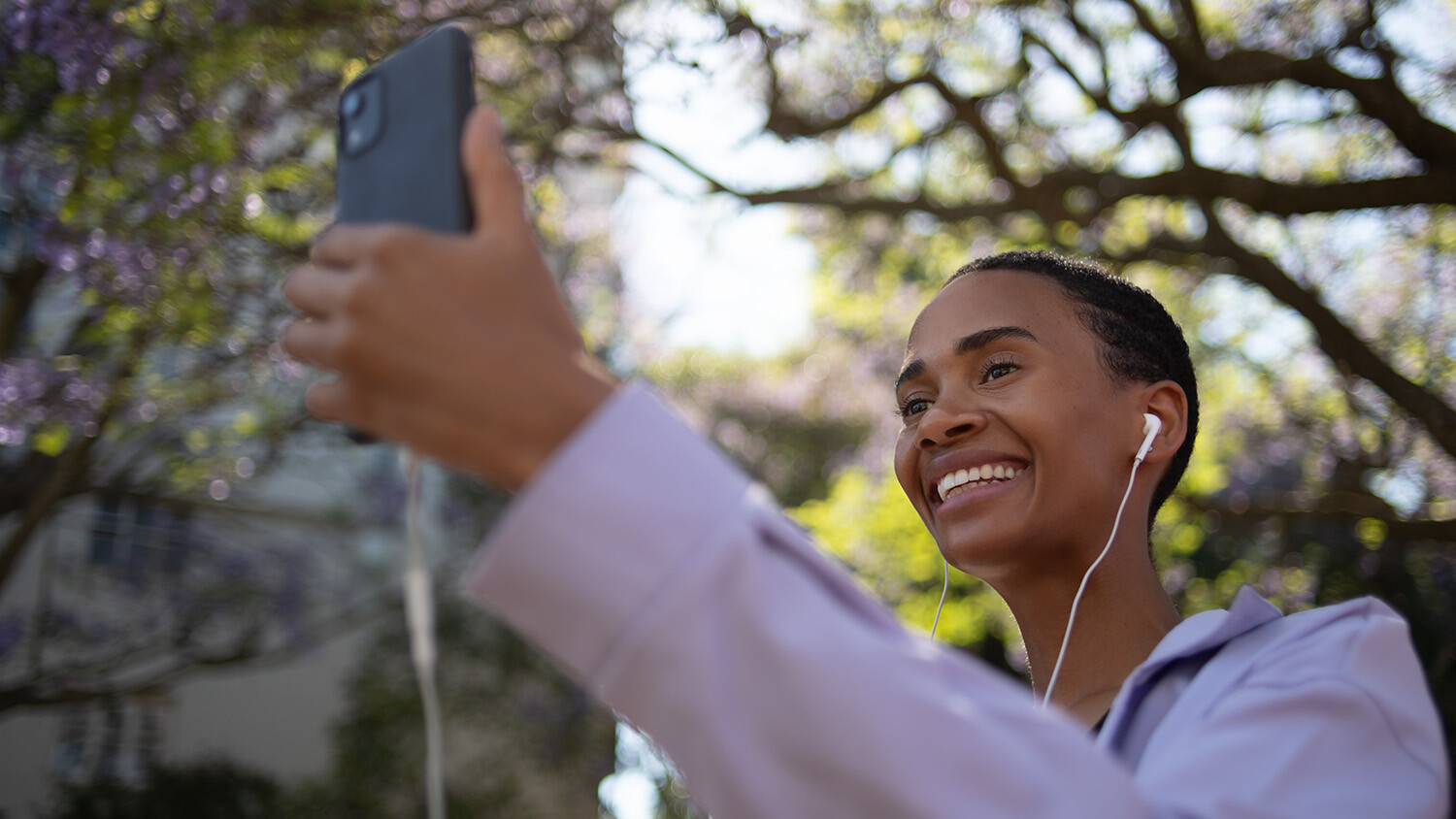 Woman video calling with phone under blooming trees.