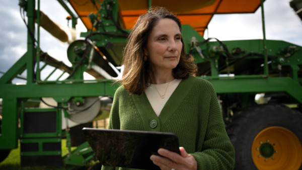 A farmer with a tablet in front of a tractor.