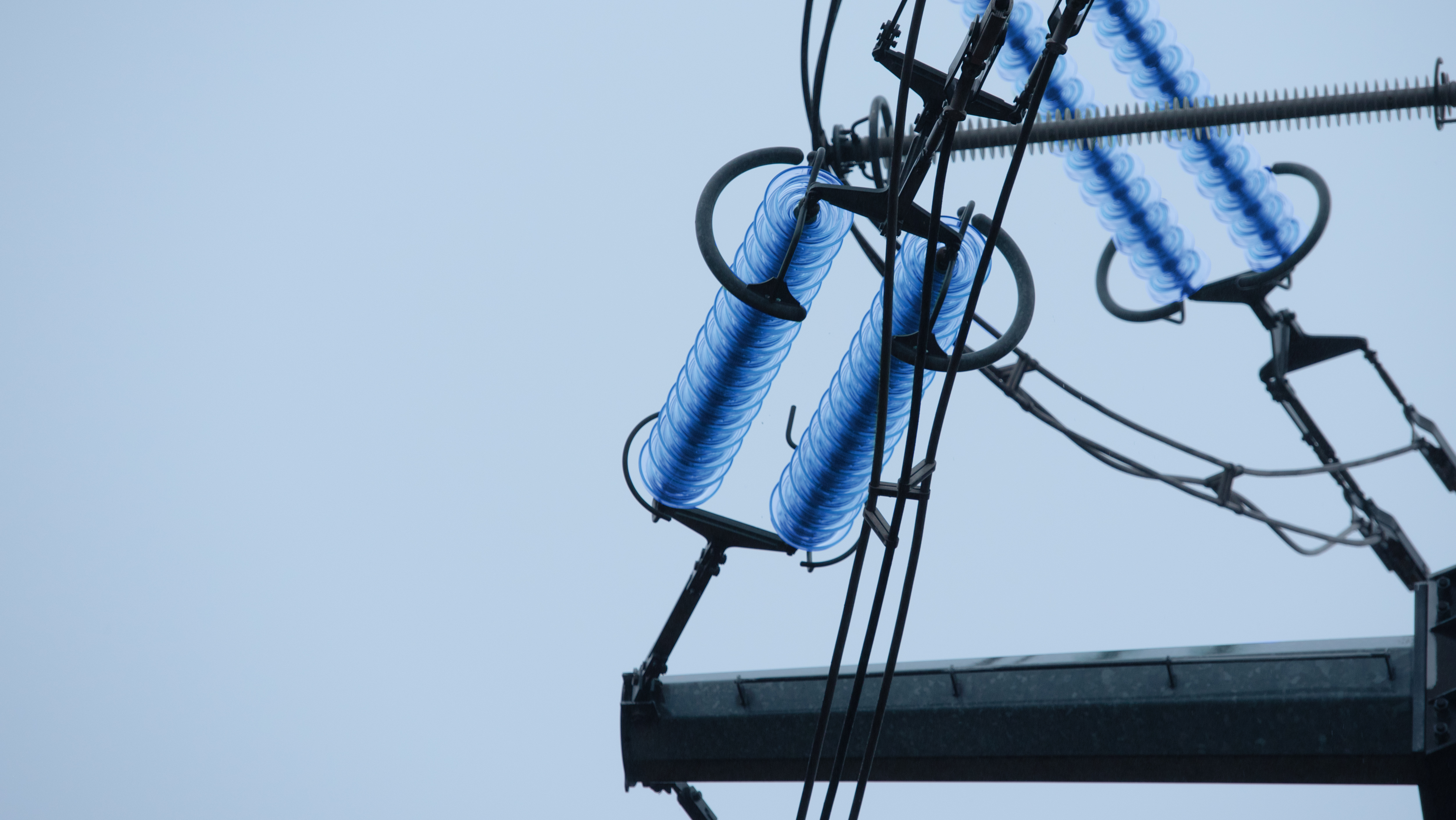 Close-up of blue-tinted electrical insulators on power line structure.