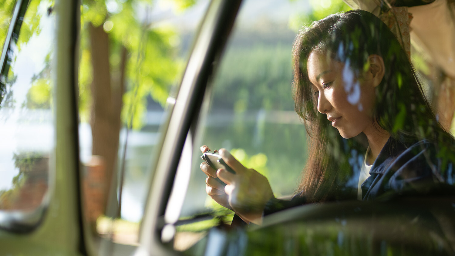 Woman uses smartphone in van with nature view.