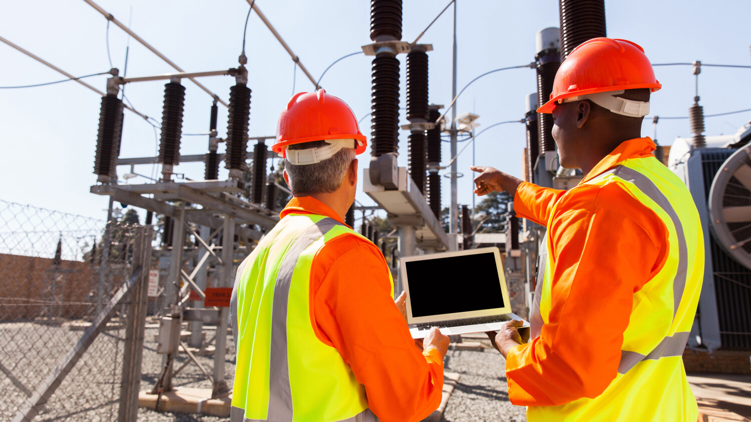 rear view of electricians with laptop pointing at substation
