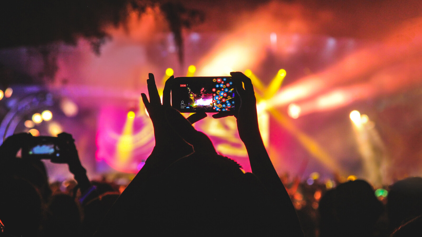 A person holding a mobile device filming at a concert.