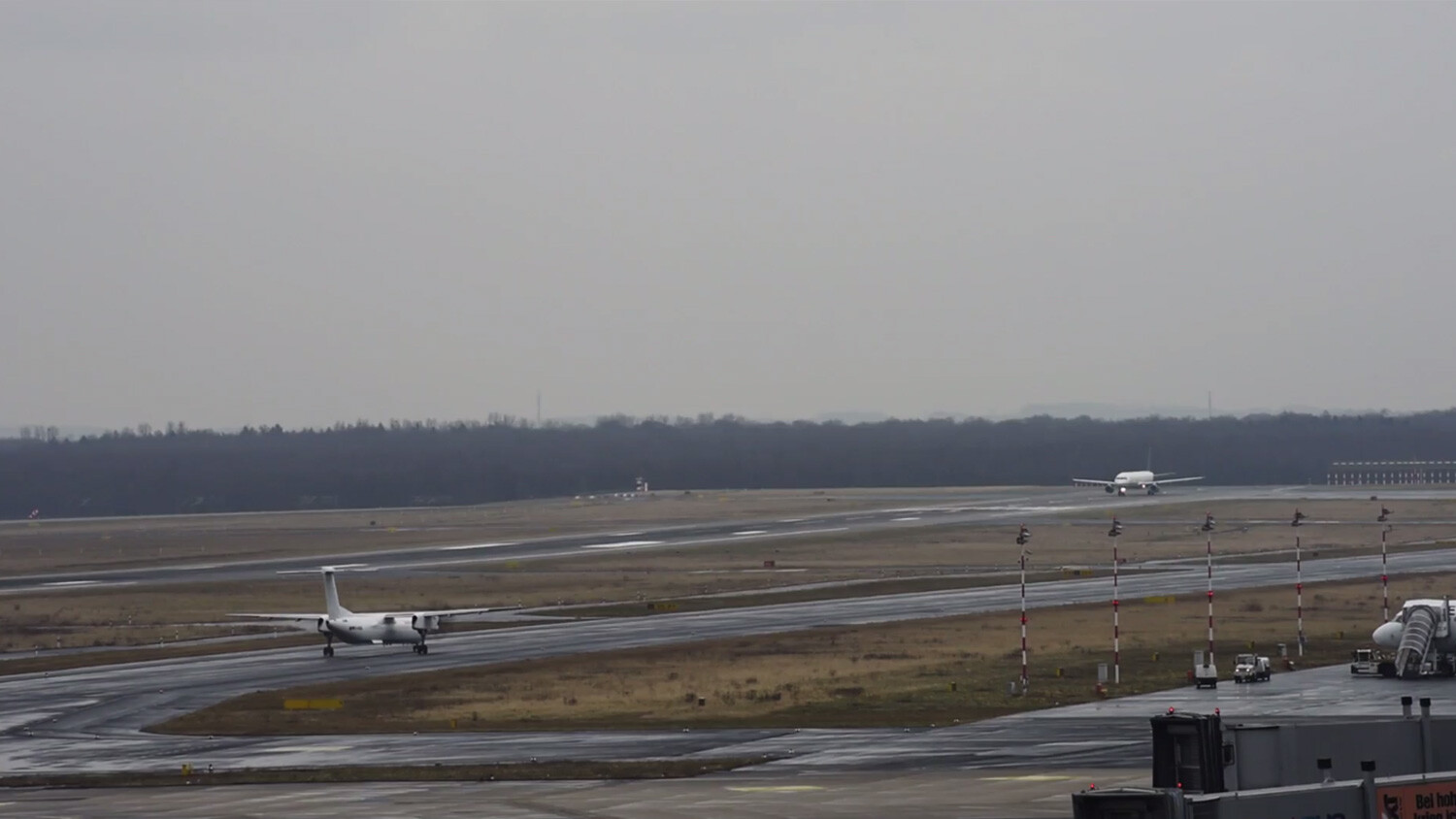 Two planes on runway, one taxiing, one landing or taking off.