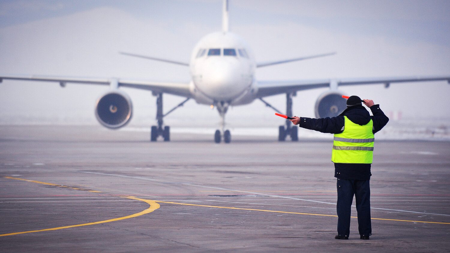 Airport worker signaling to an air plane.