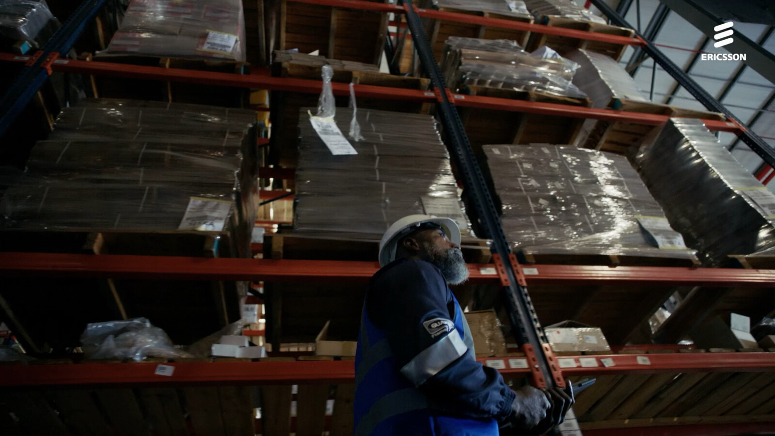Worker in safety gear inspecting stacked pallets in a warehouse.