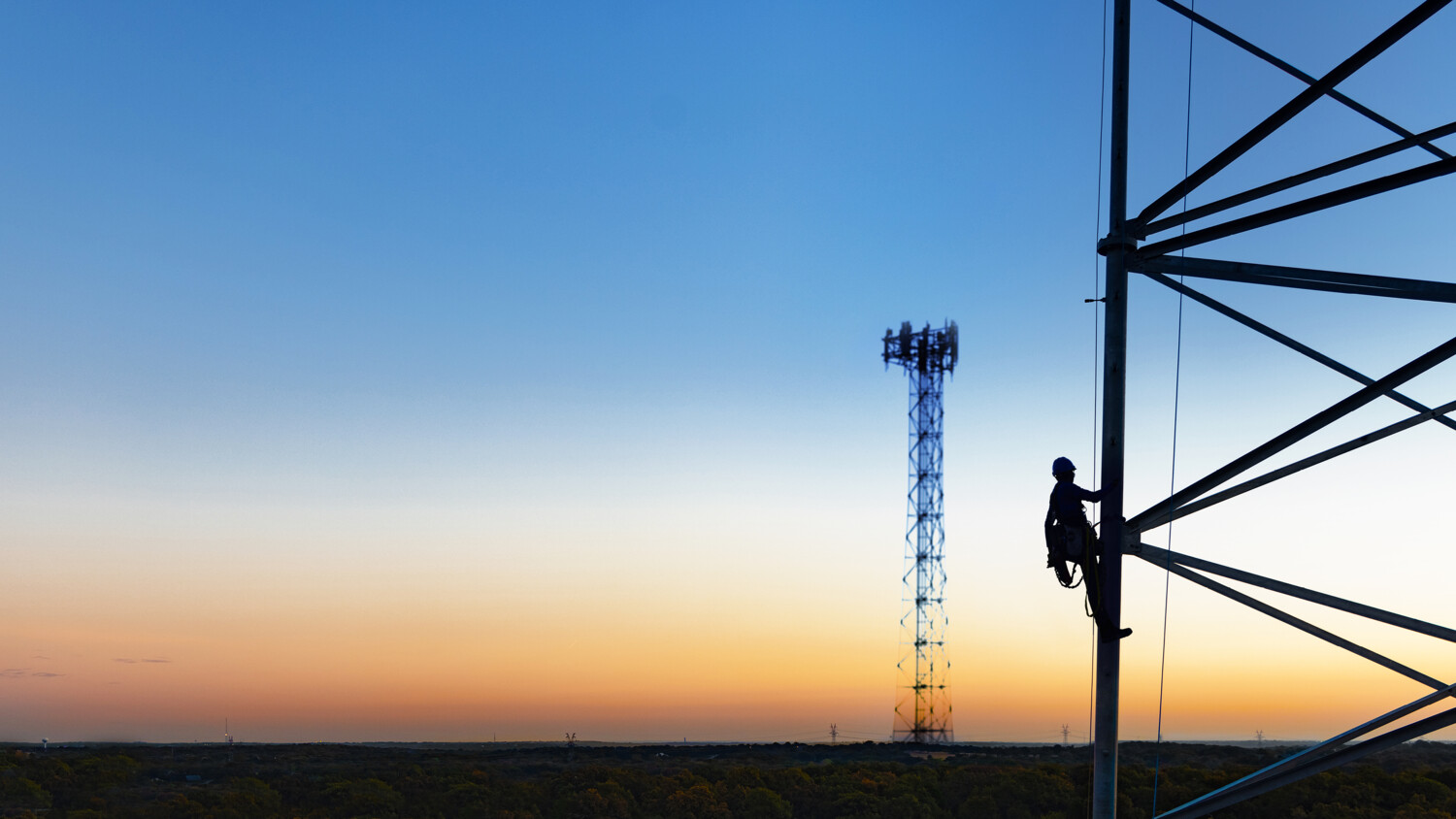Person climbing telecom tower at sunset.