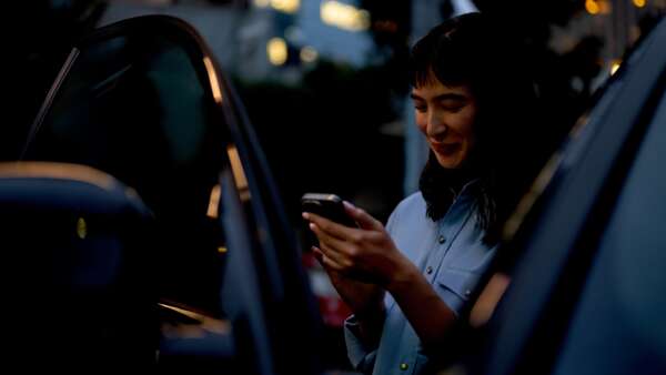 A woman getting out of a car and checking her phone