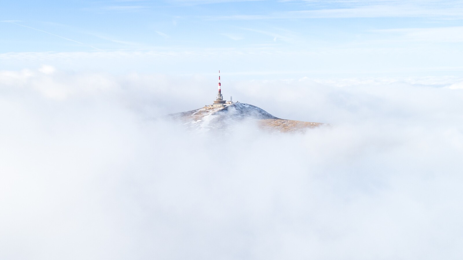 Radio tower on mountain peak surrounded by drifting clouds.