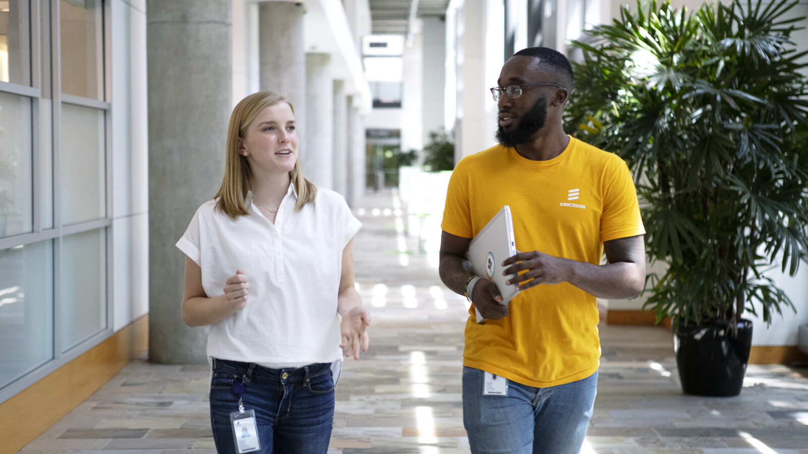 Two people walking down a hallway talking.