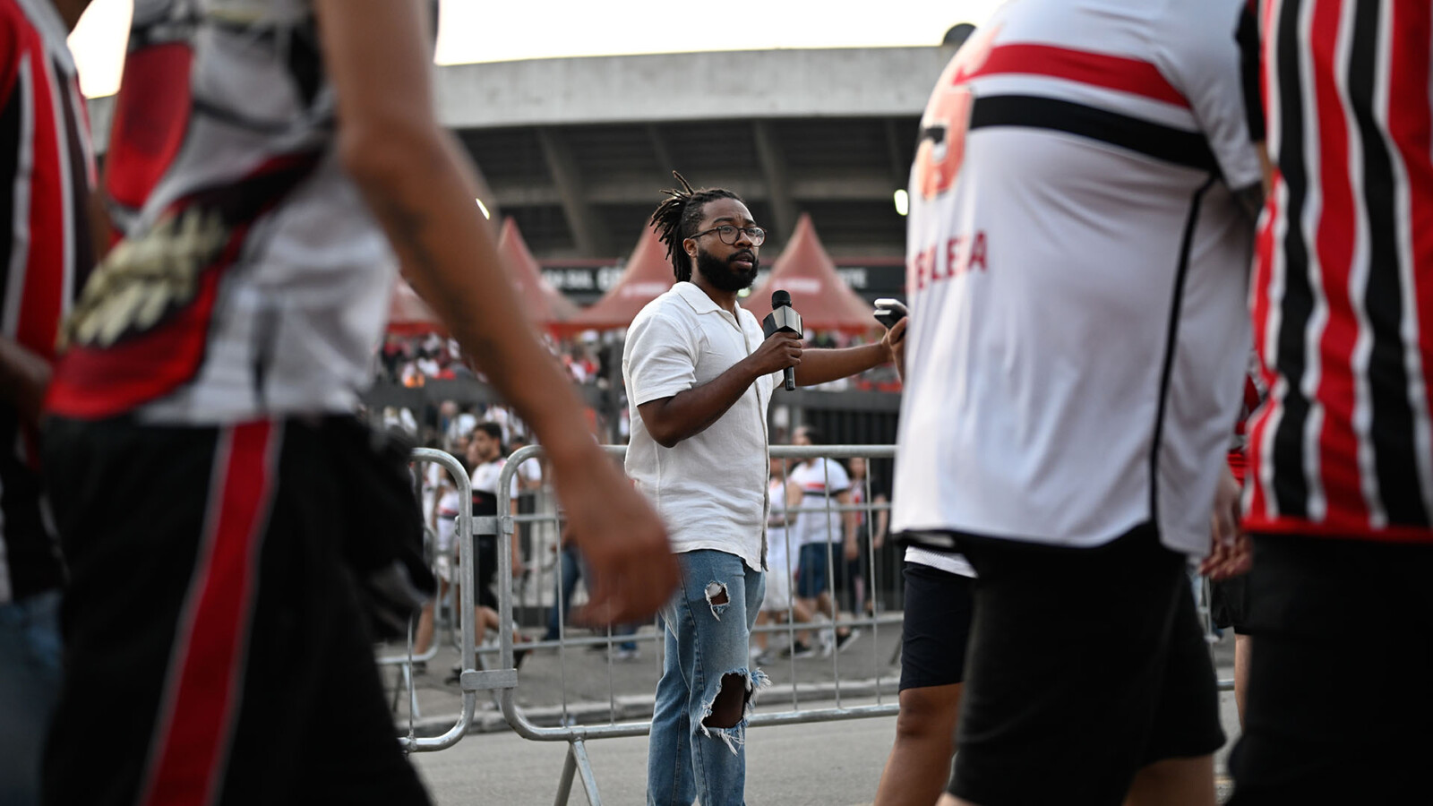 一名男子拿著麥克風在球場外採訪球迷