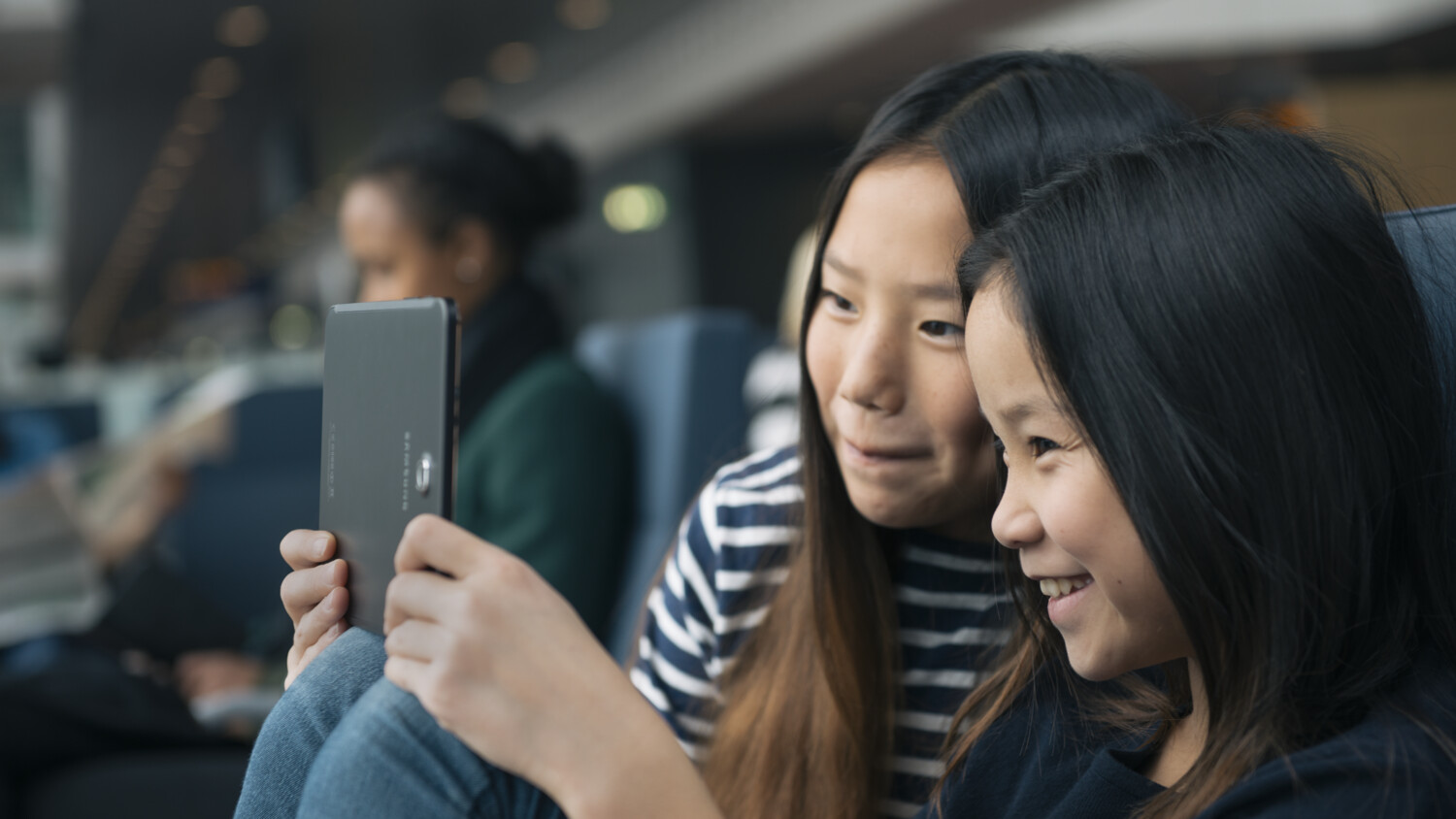 Two young girls sit smiling while looking at a tablet