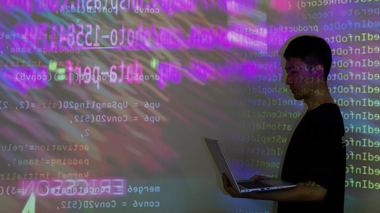 Man in front of code projection with laptop.