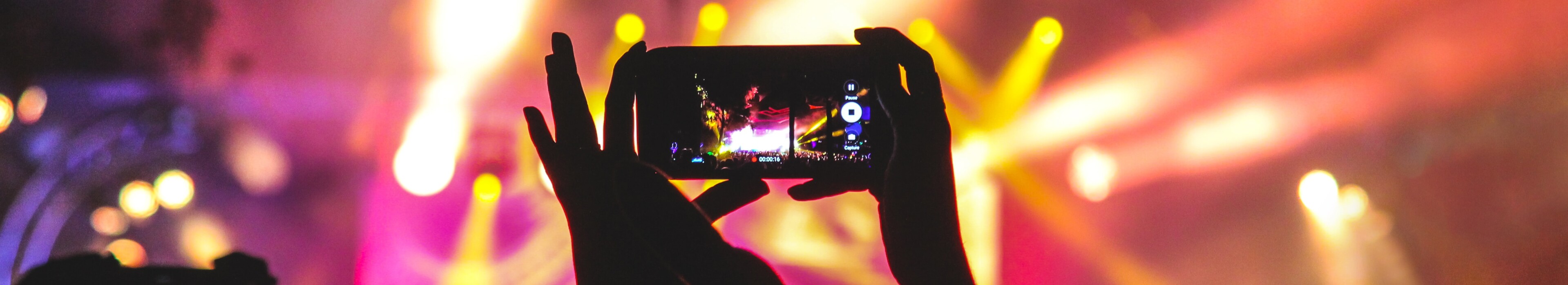 silhoutte of a person at a music concert holding up a phone and filming