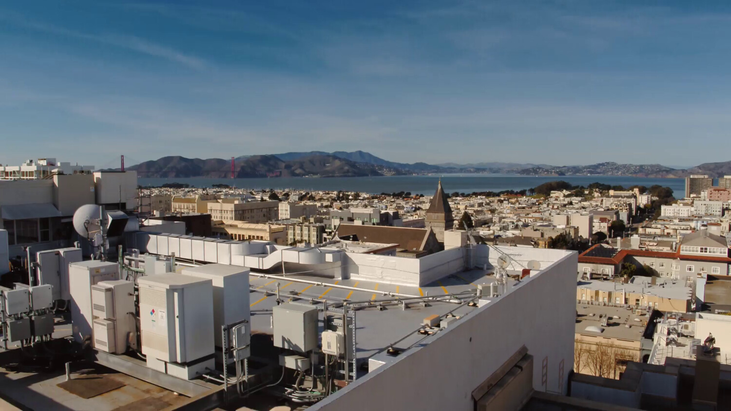 View from radio tower, cityscape with water and mountains under clear sky.
