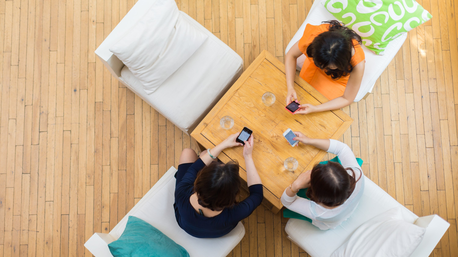 Tres mujeres sentadas alrededor de una mesa, usando sus teléfonos.
