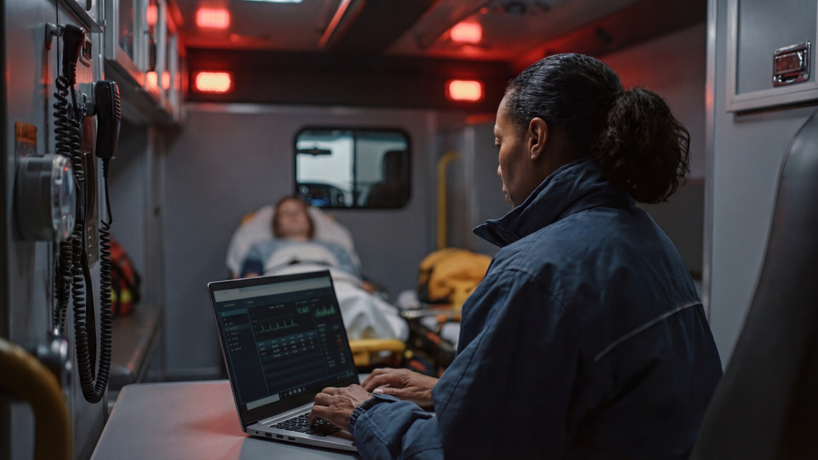 AI-generated Paramedic using laptop while monitoring patient on stretcher inside ambulance
