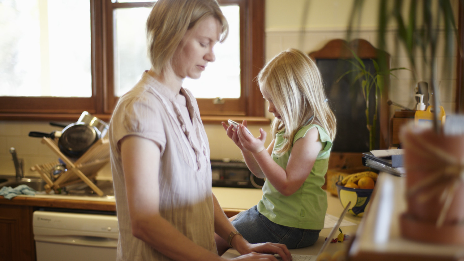 Uma mãe e sua filha nova usando seus dispositivos enquanto estiveram na cozinha.
