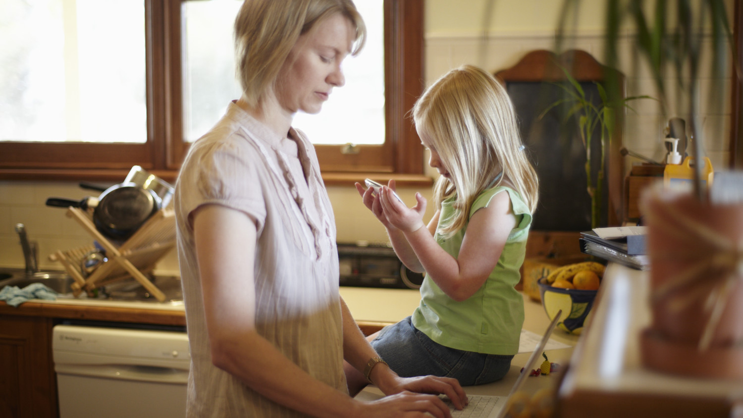 Una madre y su hija usando sus dispositivos mientras que en la cocina.