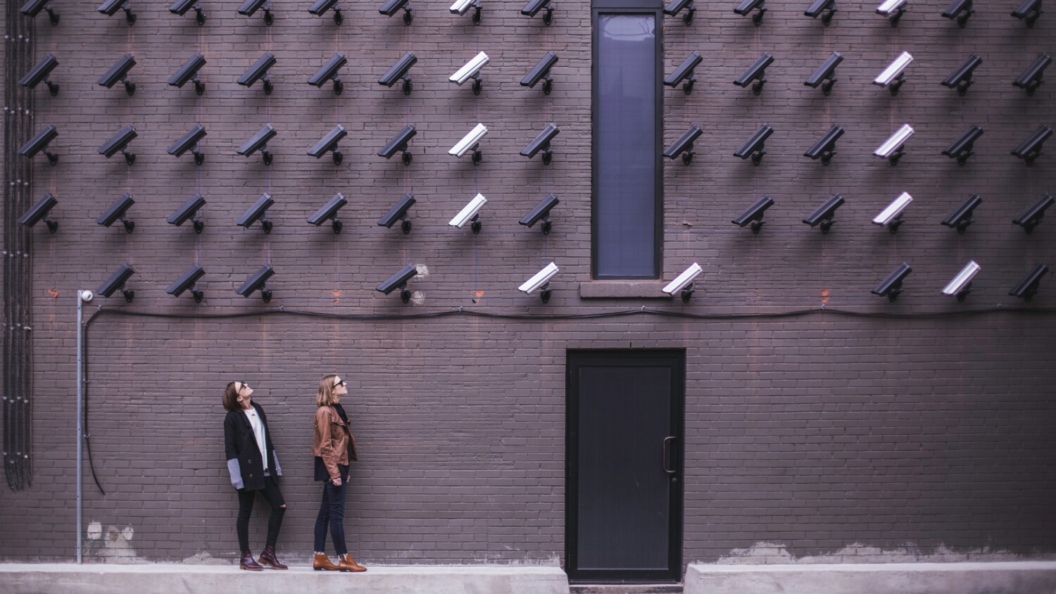 Surveillance cameras mounted on a wall pointing at two persons.