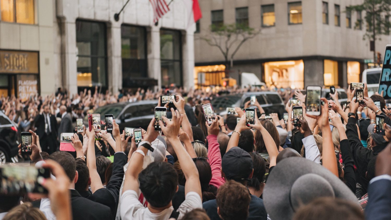 Uma rua lotada em Nova York durante a chegada do Papa. A multidão segura seus celulares para tirar fotos.