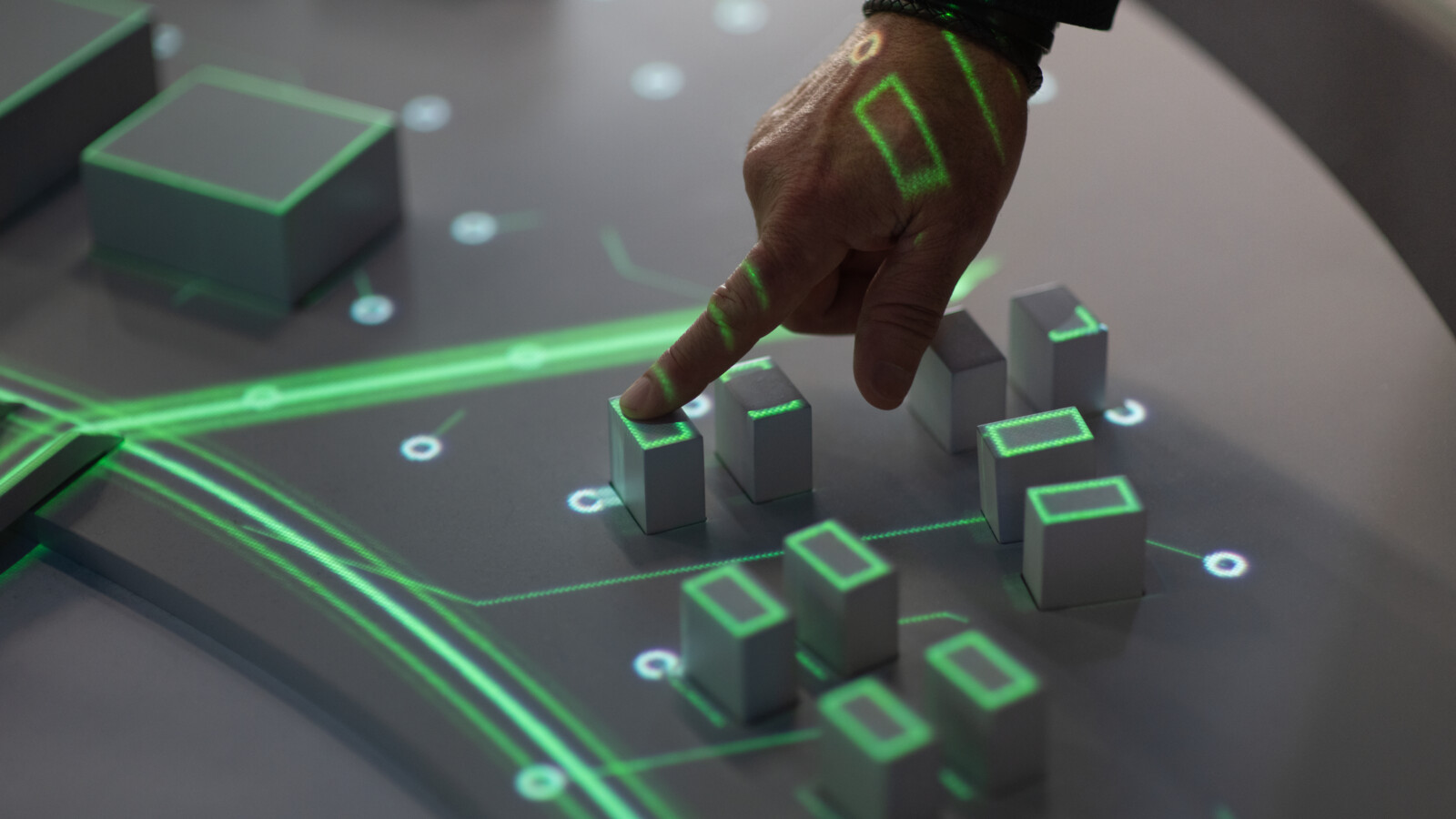 Hand interacting with AR display of small building models.