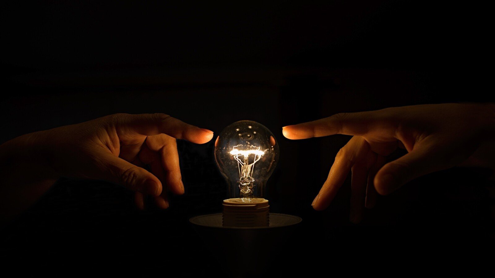 Hands reaching out to a light bulb
