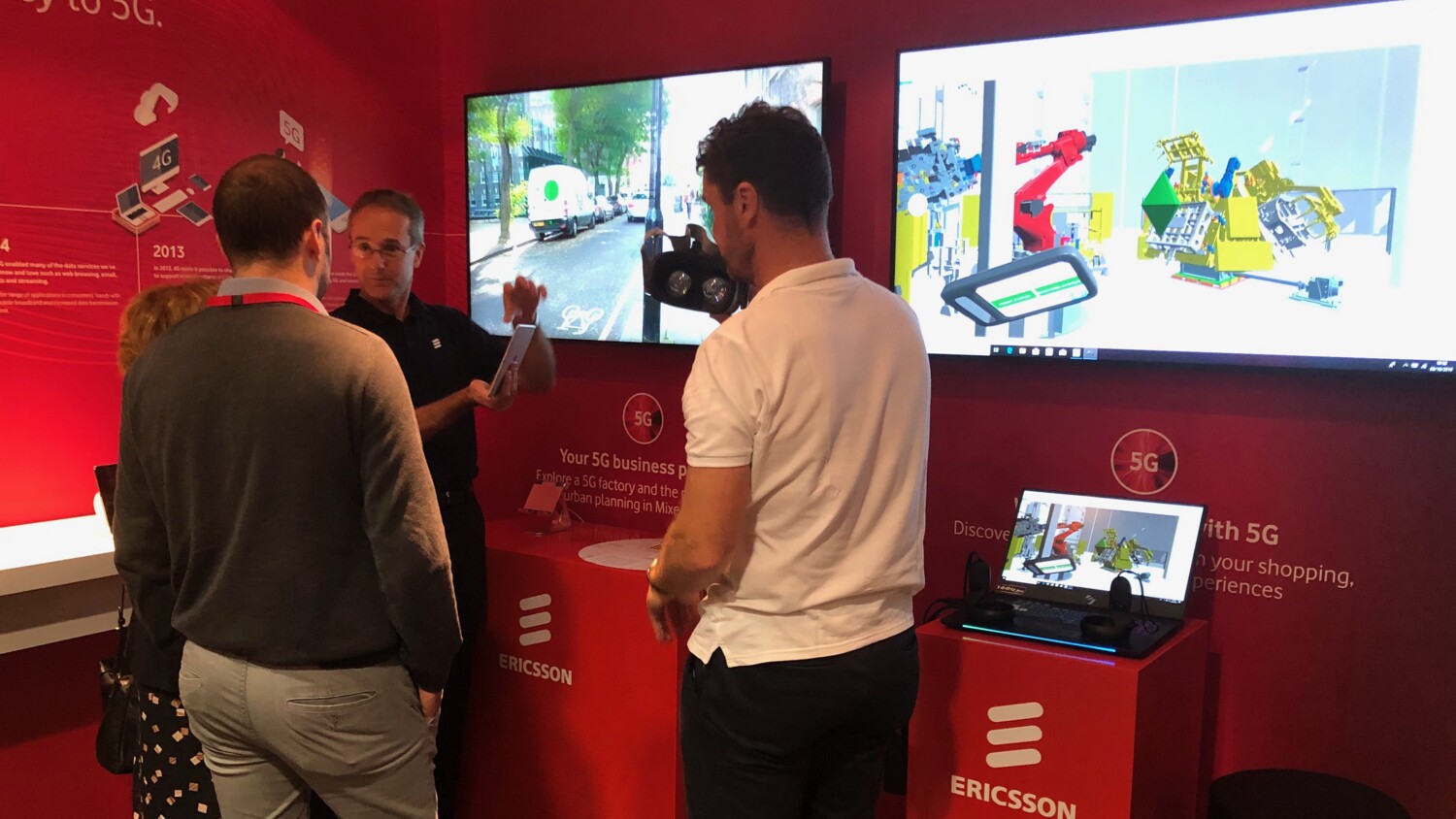 Four people looking into screens to view a demo with Ericsson logos on the stands