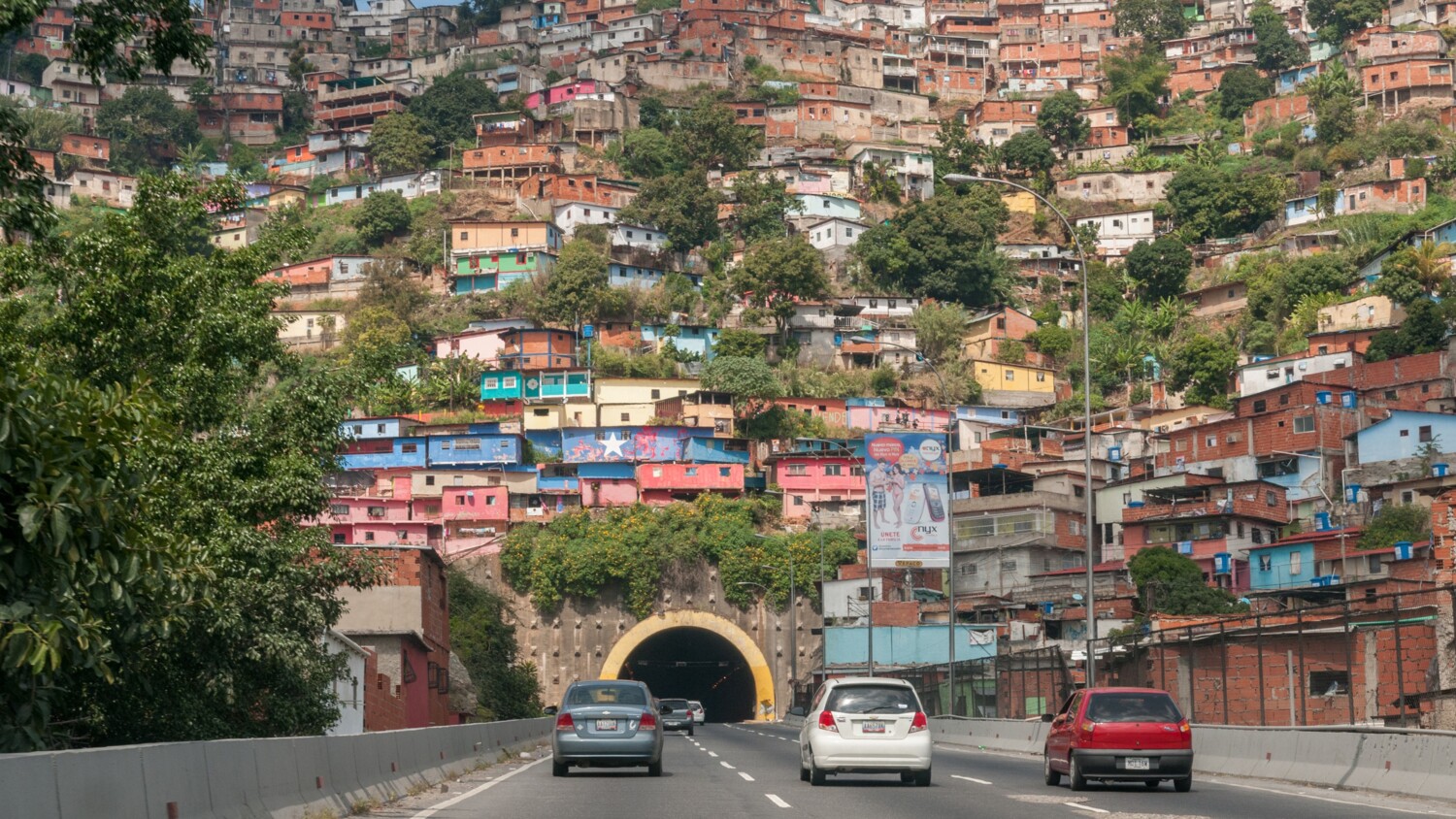 Cars approach tunnel below hillside of colorful houses.