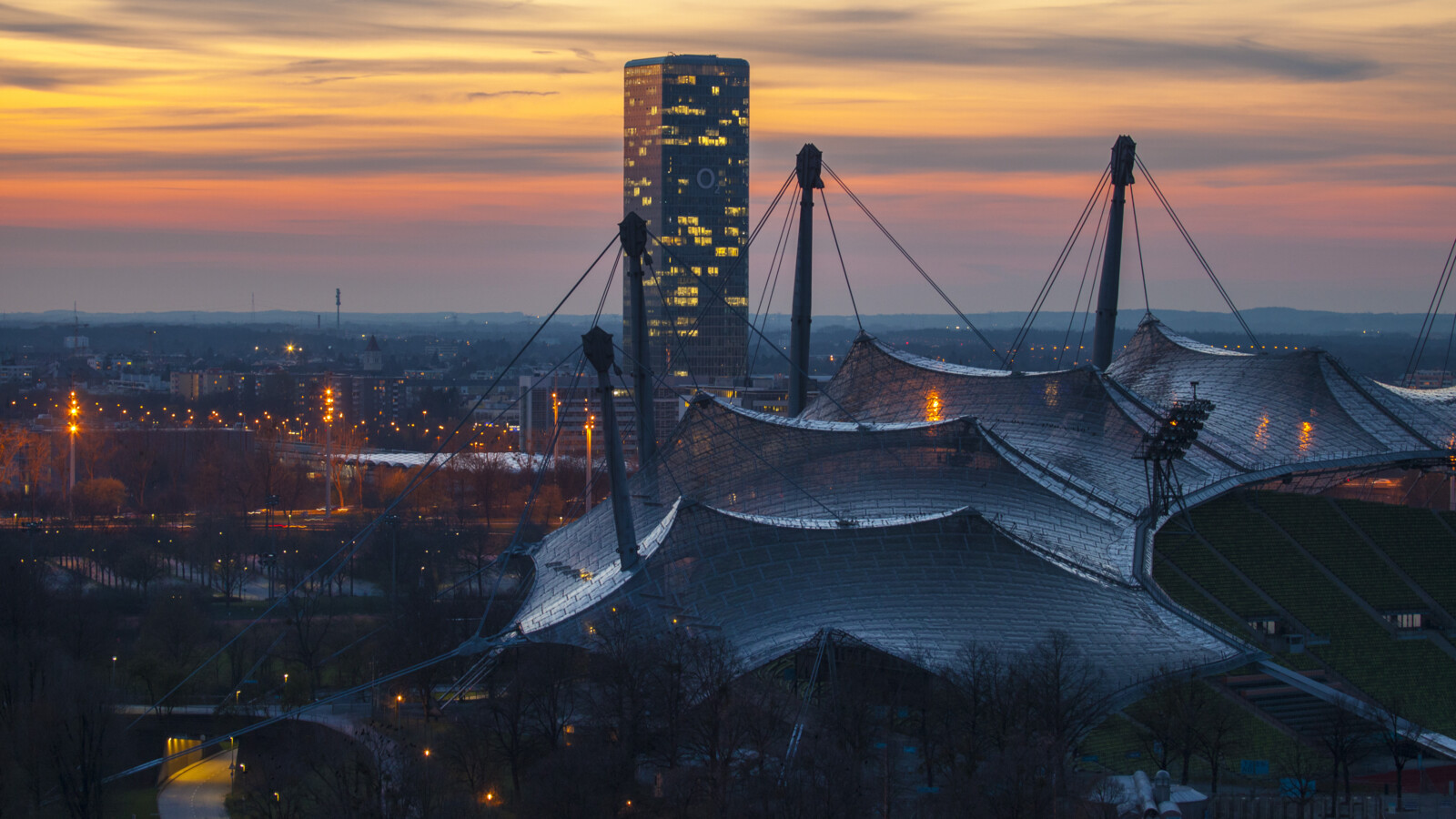 City at dusk with tent-roof structure and tall building.