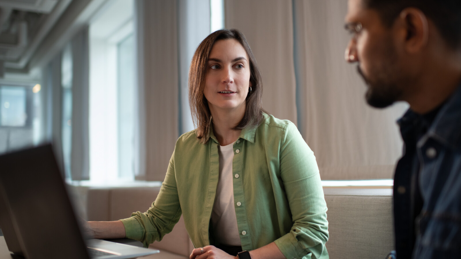 Two colleagues talking while working on their laptops.