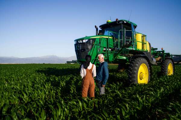 A man and a woman with a connected tractor in a field of crops
