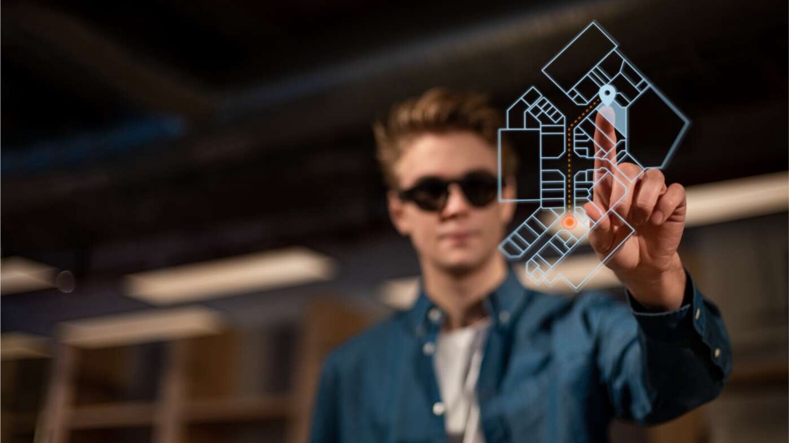 Person with AR glasses points at floating screen with floor plan display.