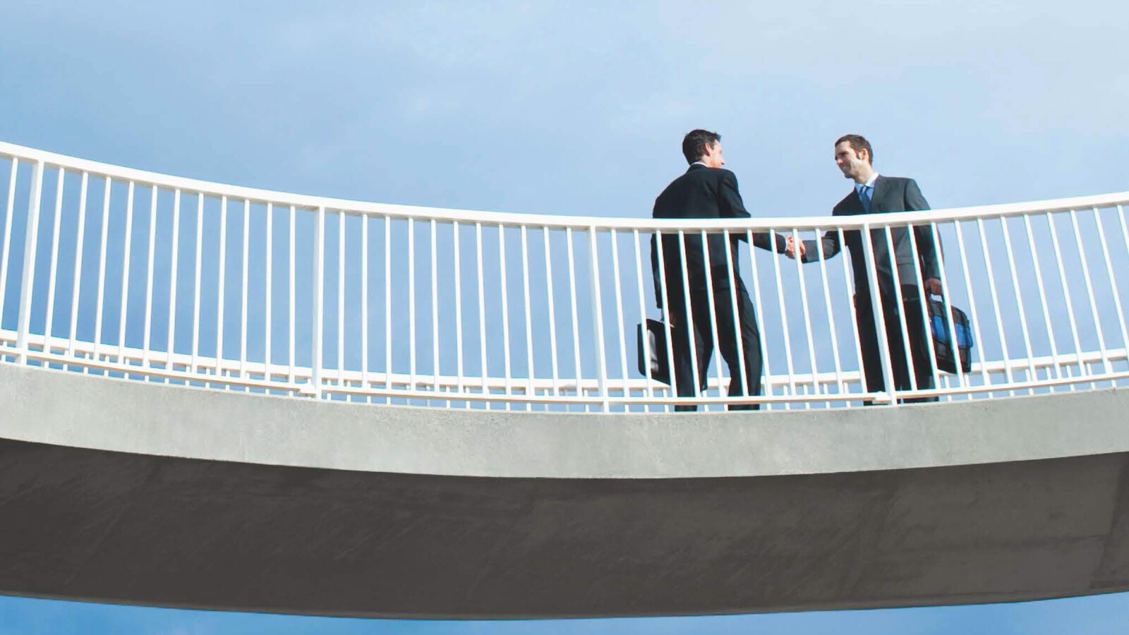 Two persons shaking hands on a bridge.