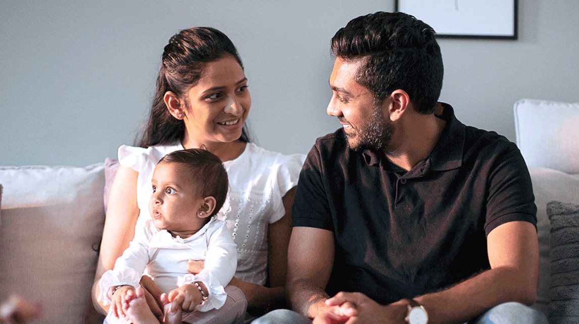 Milap and his wife sitting on a sofa with their baby child