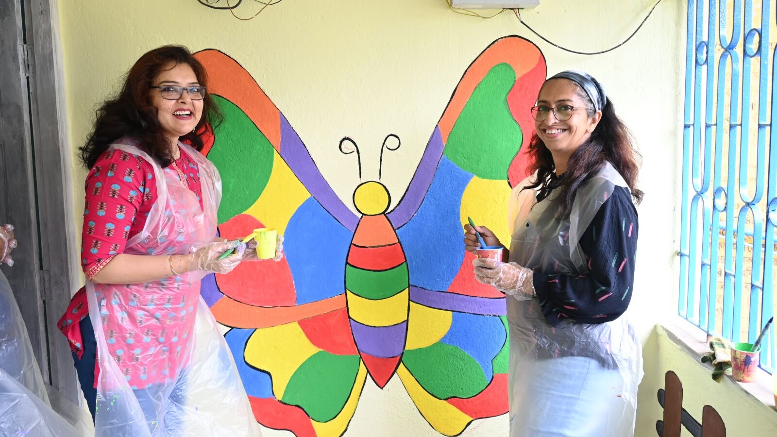 Rupa and her colleague next to their painted butterfly mural in Kolkata, India.