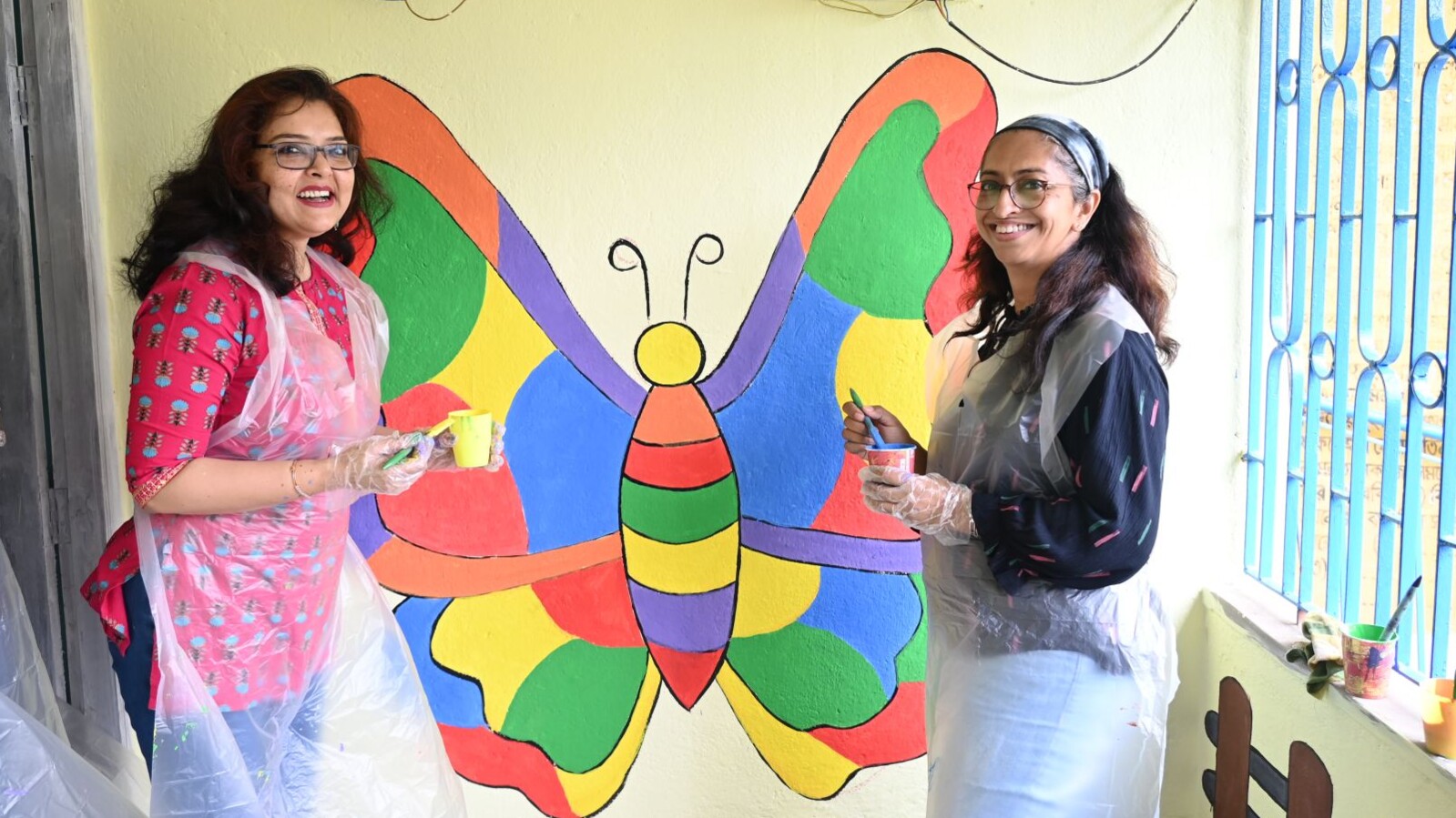 Rupa and her colleague painting a butterfly mural at a local school