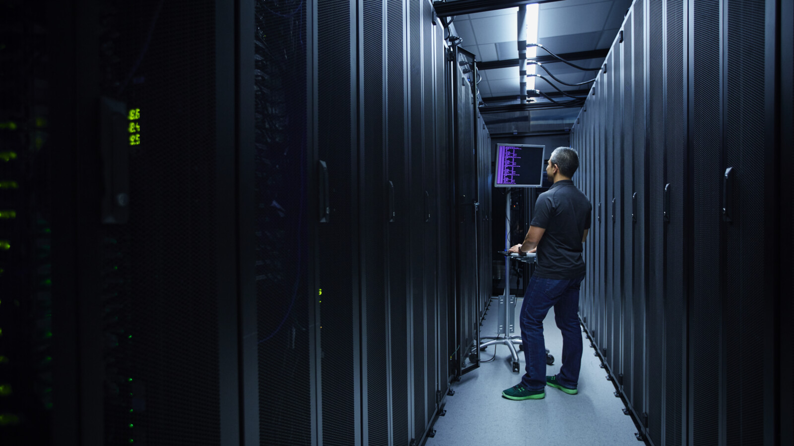 Man in server room looking at a screen.