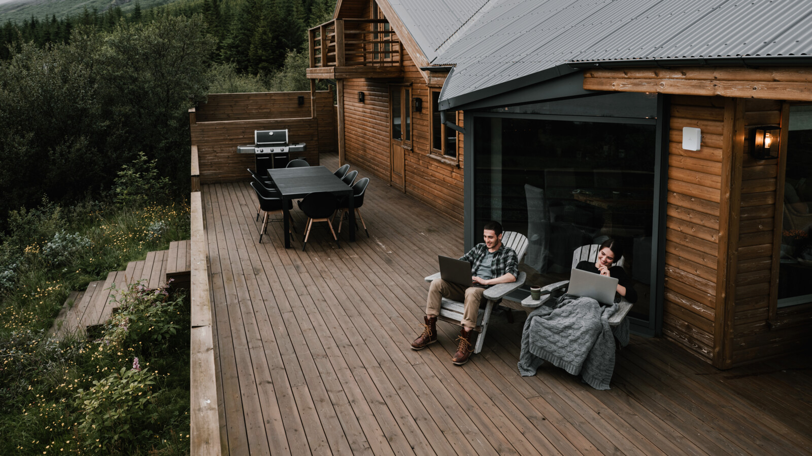Two people using laptops on deck outside a cabin.
