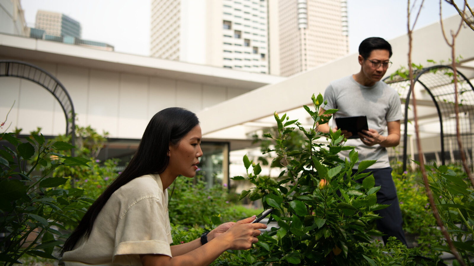 Man with a tablet and woman holding mobile in a garden in front of a building.