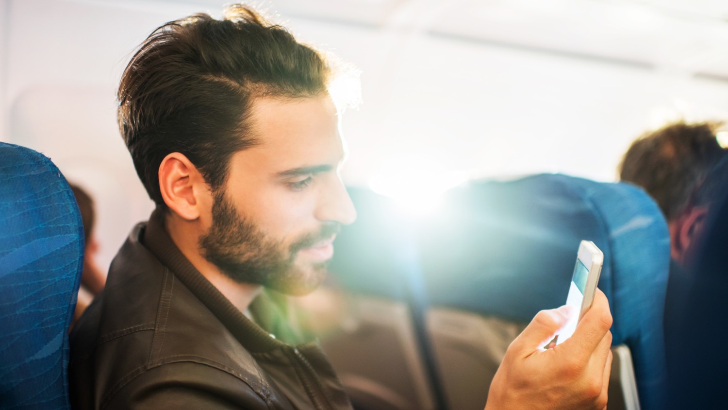 A man travelling on a commercial airplane browsing a smartphone