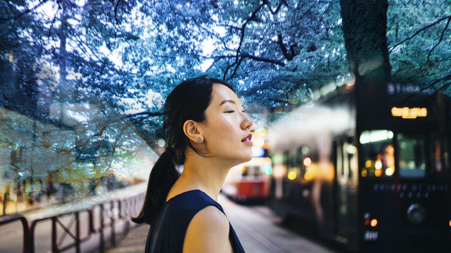 Person at city tram stop, surrounded by blue trees to illustrate internet of senses.