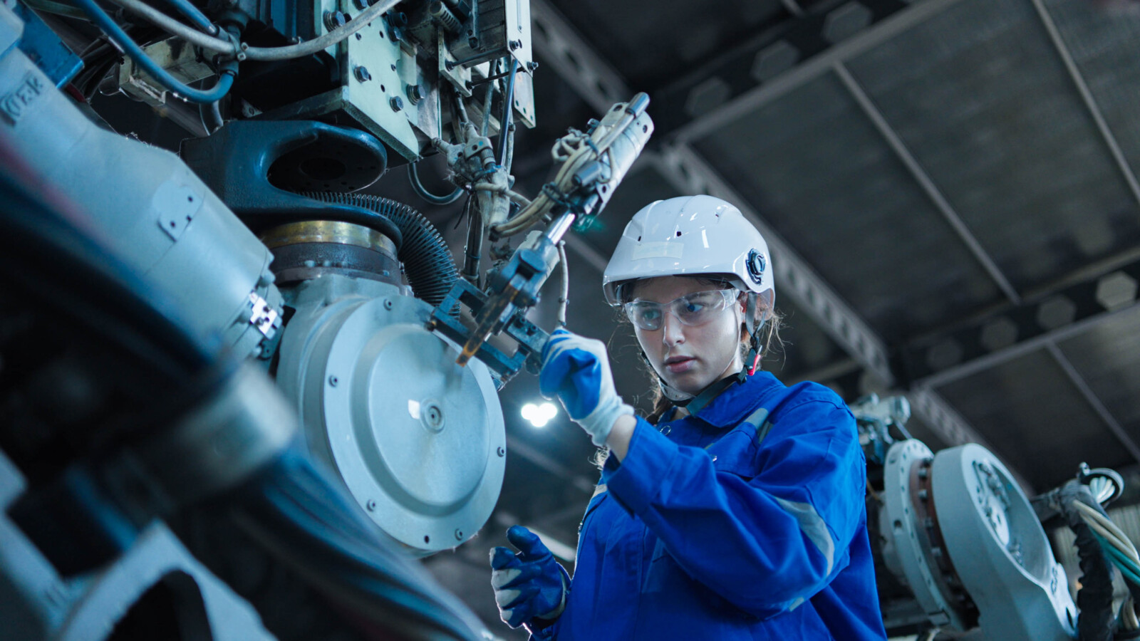 Engineer in blue uniform and helmet working on factory machinery.